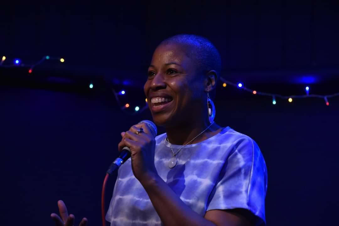 Sarah Elliott holding a mic smiling to the audience (off image)